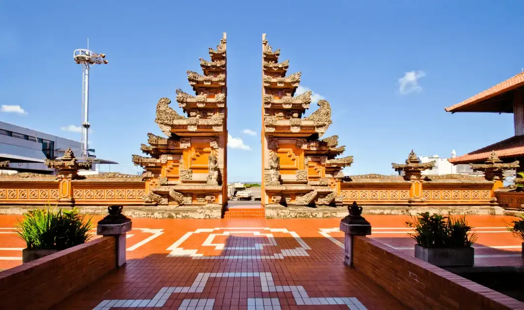 Traditional Balinese Candi Bentar split gate with intricate stone carvings and red brick courtyard at Ngurah Rai Airport, Bali